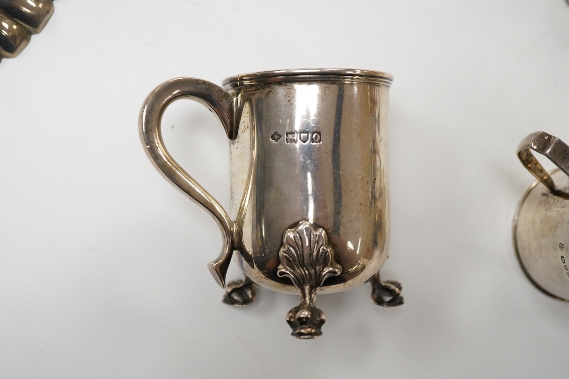 An Edwardian silver mug, on claw and hoof feet, William Hutton & Sons, London 1909, height 83mm, together with a silver butter shell, mustard pot and a silver five bar toastrack, 17oz.
